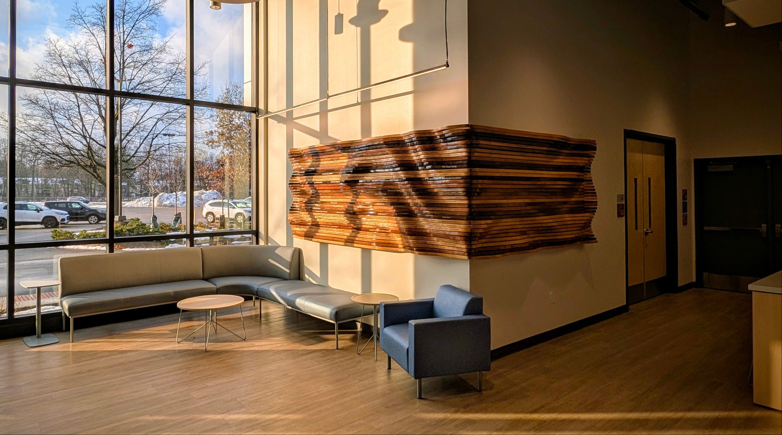 Traverse City Philharmonic Center wavy Parametric wall art installation flowing from one wall to the next with names on the slats made from solid wood stained in different colors with smooth finish. 